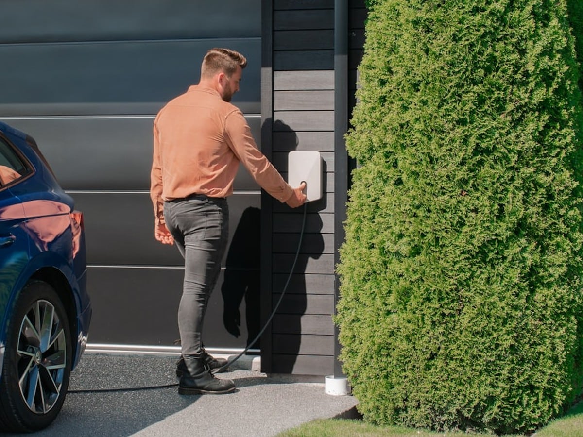 Homeowner scheduling EV charging next to a blue electric vehicle in the driveway