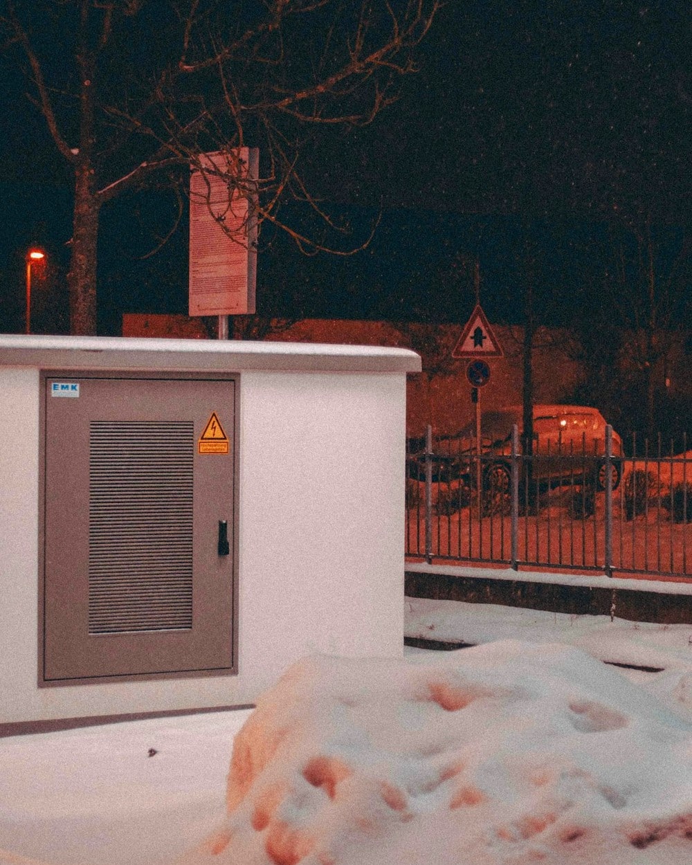 Snow-covered electrical box beside a bare tree on a winter night