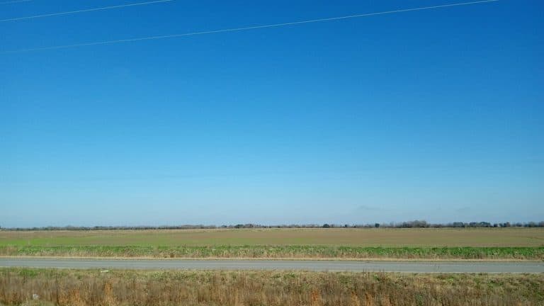 Empty two-lane road through open fields under a wide sky in rural Texas