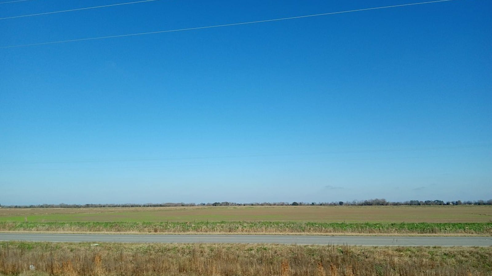 Empty two-lane road through open fields under a wide sky in rural Texas